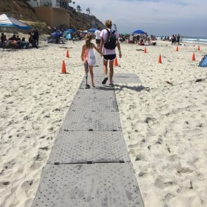A mom and daughter who uses a prosthetic leg walk on the grey Beach Trax path at the beach.
