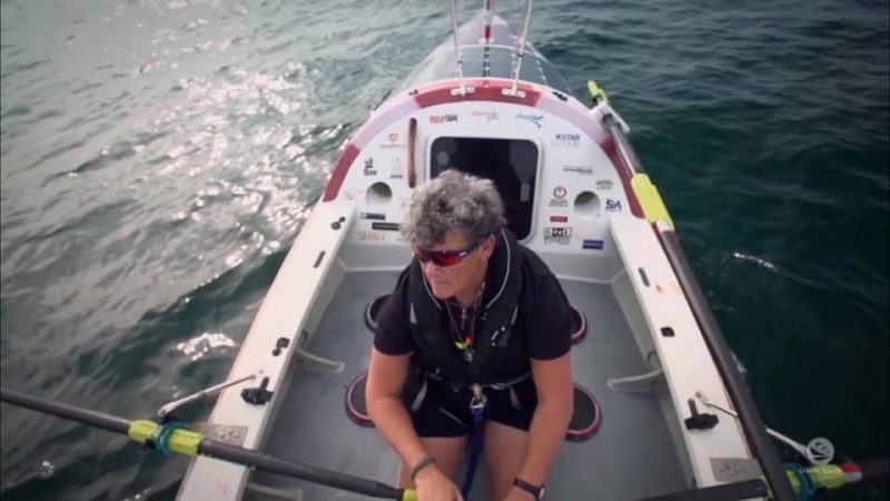 Angela, a woman in her 60s, is shown rowing in her boat in the open ocean.